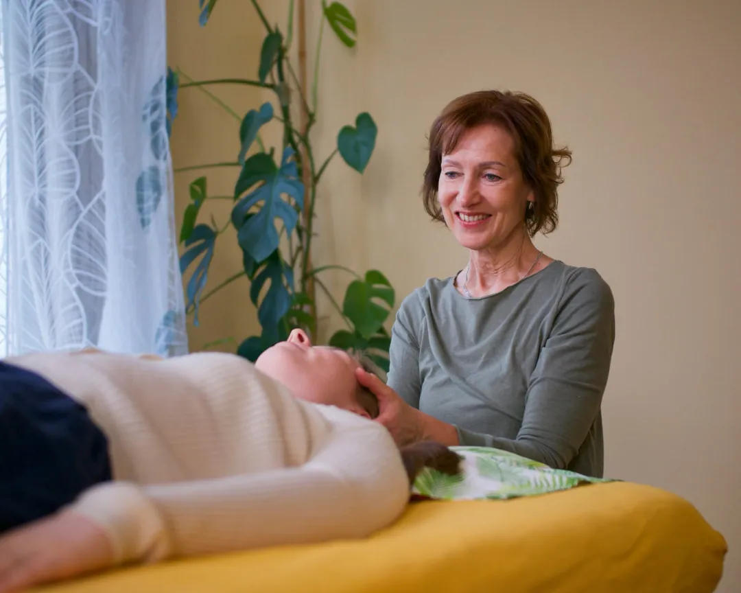 Craniosacrale Behandlung: Mag. Silvia Pruckner hält sanft den Kopf einer Klientin auf der Behandlungsliege