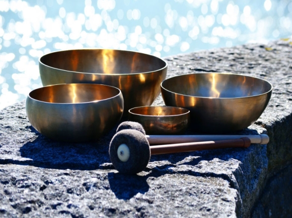 Vier handgeschmiedete Klangschalen in verschiedenen Größen mit Filzschlägel auf einem Stein im Sonnenlicht