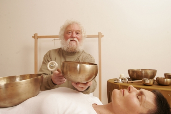 Peter Hess bei einer Klangmassage: Klangschale wird neben einer liegenden Klientin mit einem Filzschlägel angeschlagen